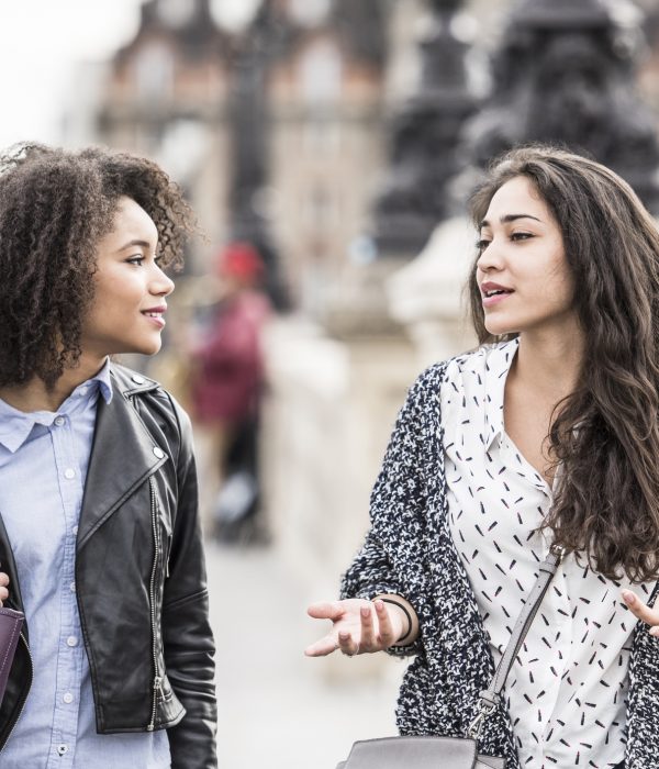 Two young women walking in Paris street having conversation. Young woman gesturing with hands, female friend listening